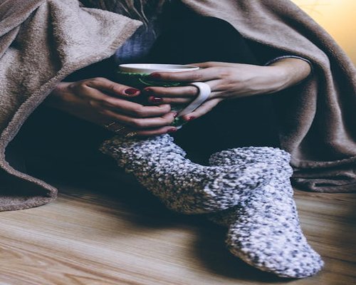 person resting feet on a soft pouf with a cup of hot tea