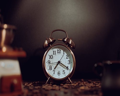 alarm clock and fresh coffee on a bedside table bathed in morning sunlight