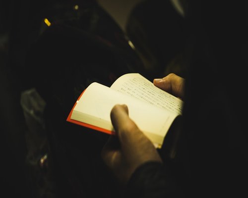 hands holding an open book under a warm reading lamp light