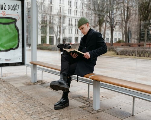 person waiting at a bus stop in autumn clothes reading a book